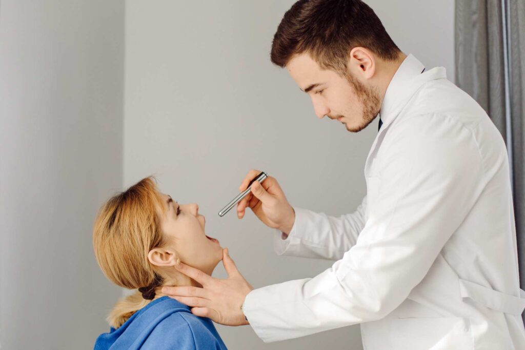 ENT specialist performing a throat examination on a patient to identify the causes of voice disorders affecting vocal cord function and voice quality.